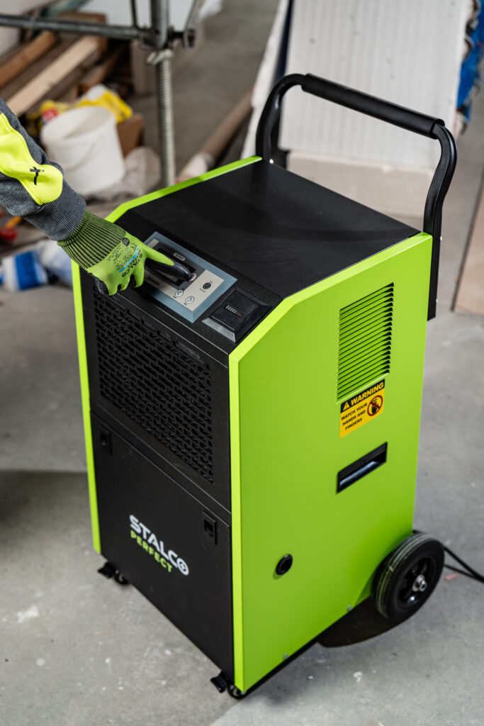 Ruka remeselníka v ochrannej rukavici nastavuje parametre sušenia na ovládacom paneli stavebného odvlhčovača STALCO PERFECT.