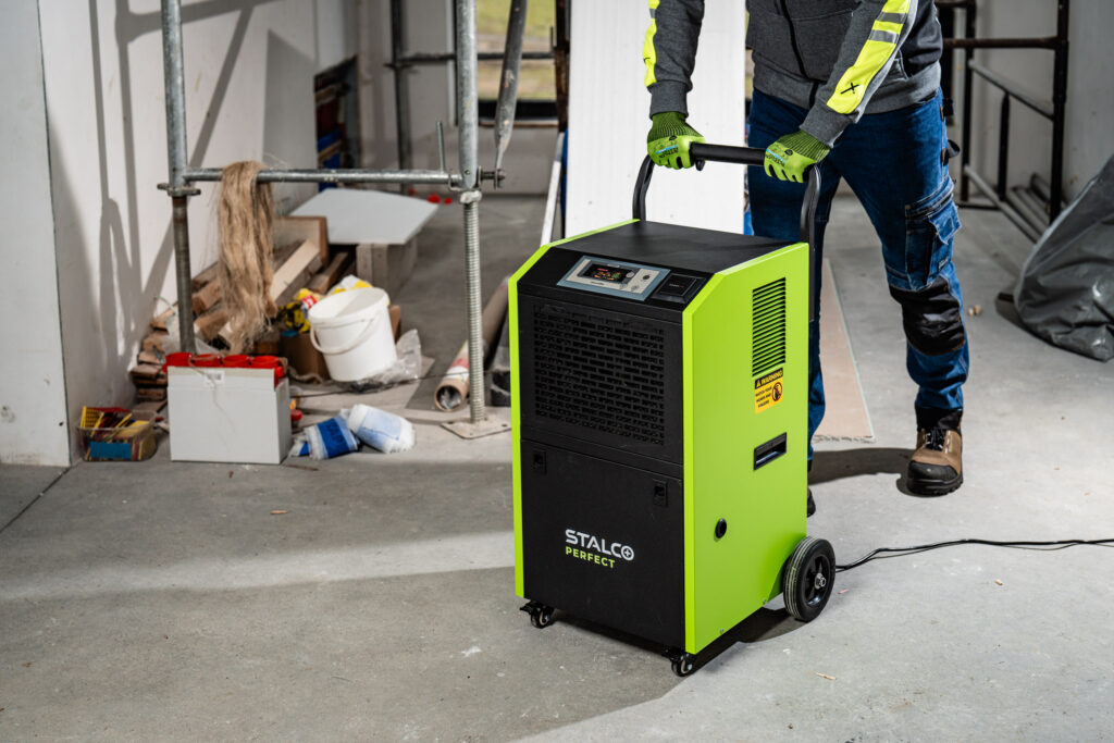 Pracovník pripravuje profesionálny stavebný odvlhčovač STALCO PERFECT na vysúšanie hrubej stavby po mokrých procesoch.